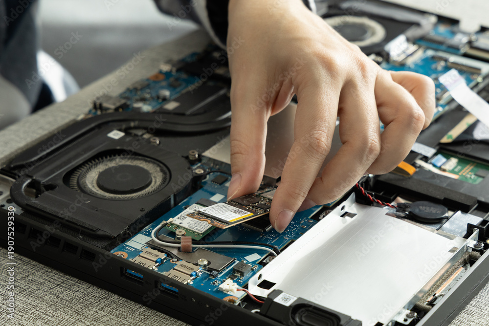 Naklejka premium Person Works on Laptop Hardware Repair in a Modern Setting During Daylight Hours