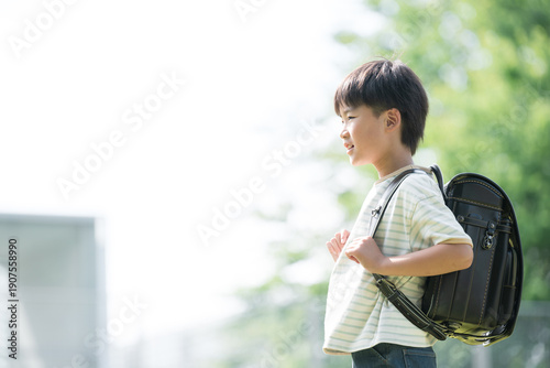 Schilderij op canvas 学校の校舎と緑を背景に校庭でランドセルを背負って走る少年の(男の子)男子の横顔、逆光の未来や希望を見つめるスタートするイメージ　コピスペースあり