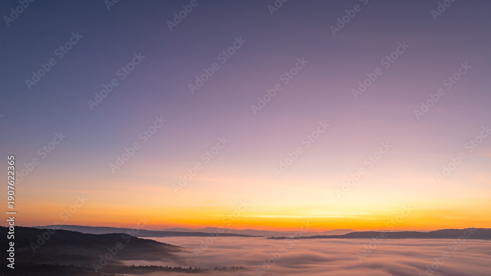 Obraz premium A stunning aerial landscape of sunrise over mountains wrapped in soft fog, perfect for travel, nature, and cinematic visual storytelling. Vibrant Sunrise Over a Tranquil Valley Wrapped in Morning Fog