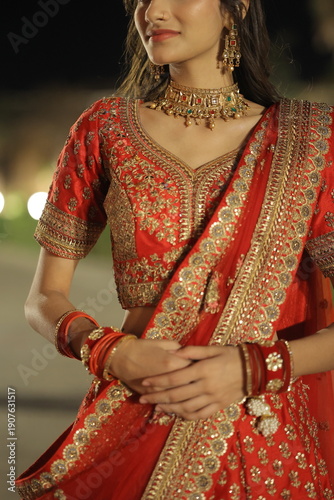 Beautiful young Indian woman dressed in an elegant red embroidered lehenga with traditional jewelry, posing outdoors at night