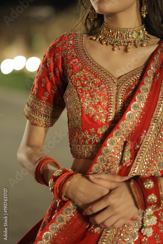Beautiful young Indian woman dressed in an elegant red embroidered lehenga with traditional jewelry, posing outdoors at night