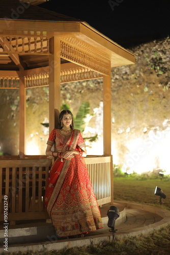Beautiful young Indian woman dressed in an elegant red embroidered lehenga with traditional jewelry, posing outdoors at night