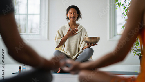 Black woman with singing bowl practicing group sound healing meditation. Concept of mindfulness, mental health, stress relief, holistic wellness and authentic self-care ritual at studio.