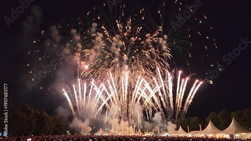 Vibrant red fireworks illuminate the night sky above a large festive crowd