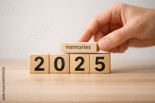 Hand stacking wooden blocks to change 2025 to memories, symbolizing past year reflection and future planning.