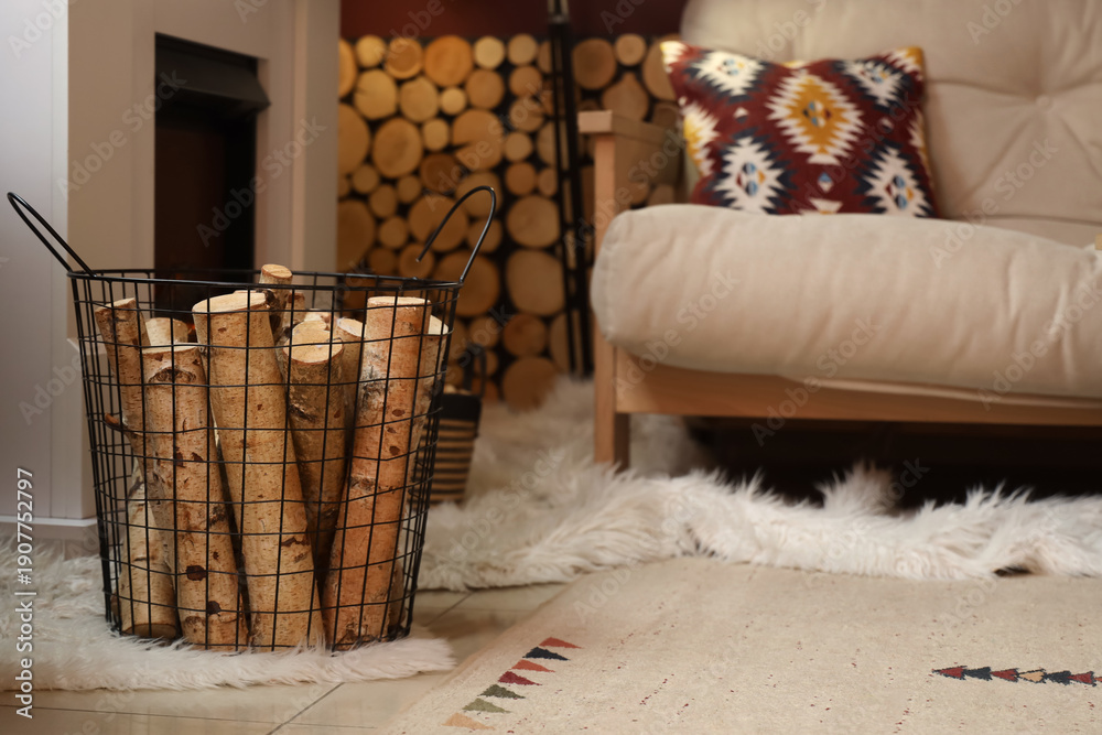 Naklejka premium Basket of firewood with sofa near fireplace in living room, closeup