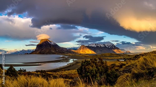 A coastal landscape with mountains, water, and dramatic clouds catching the sunrise