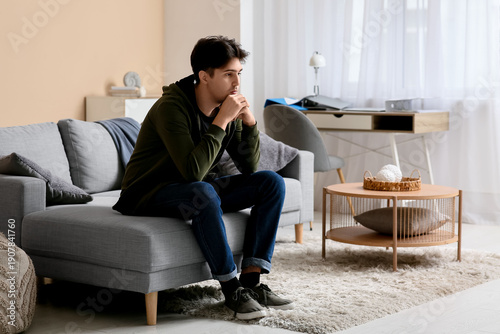 Depressed young man sitting on sofa at home