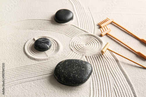 Canvas Print Black stones and small rakes on light sand with lines