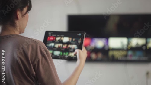 Woman streaming video on demand on a smart tv using a tablet for media consumption and entertainment