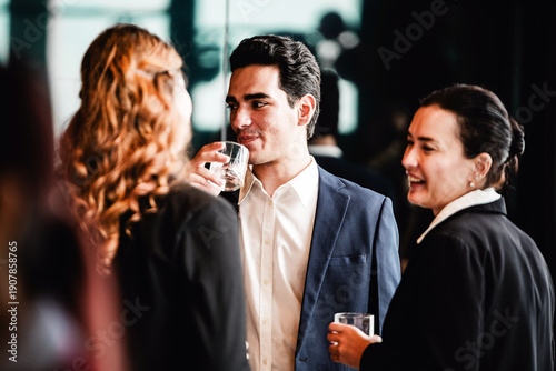 Photos Professionals in formal attire networking at a corporate event, chatting and sipping drinks in a modern indoor setting