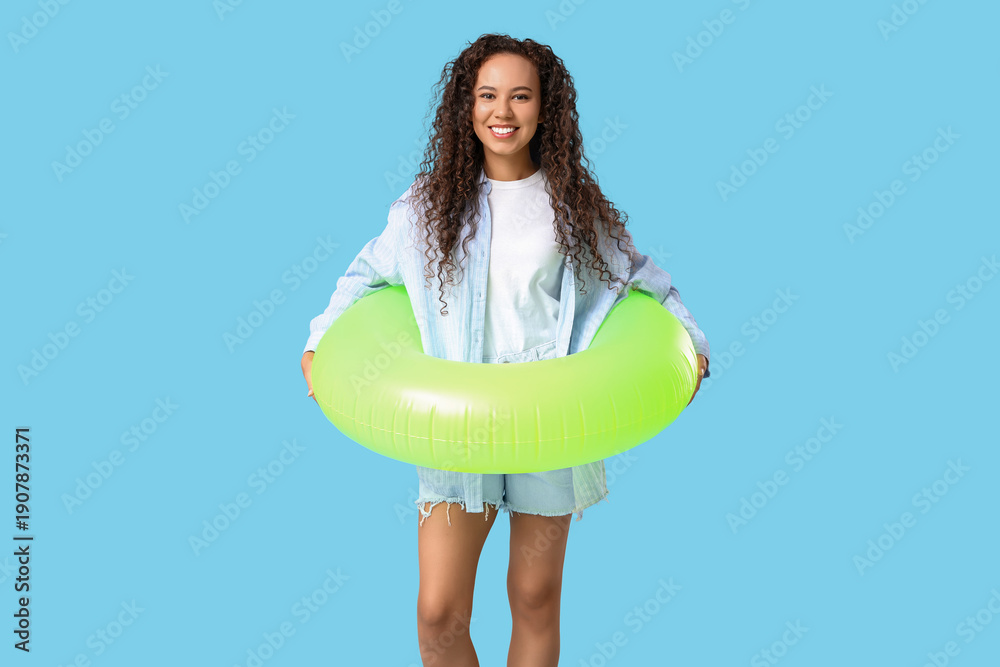 © Pixel-Shot - Beautiful young African-American woman with inflatable ring on blue background © Pixel-Shot - Beautiful young African-American woman with inflatable ring on blue background