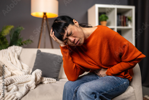 Photos Asian woman suffering from stomach ache and headache on sofa