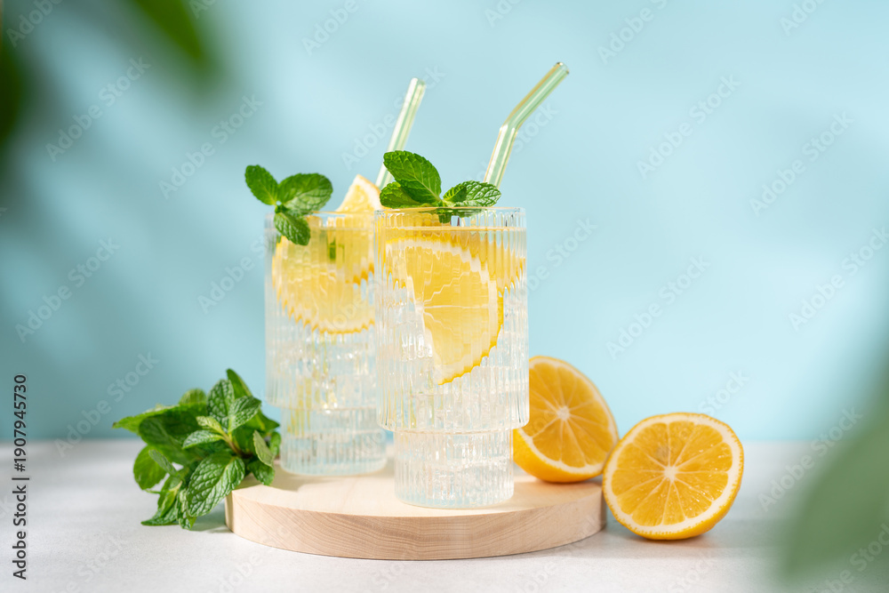 Fototapeta premium Fresh Lemonade in Tall Glass with Lemon Slice and Mint on Blue Background, Refreshing Summer Drink with Copy Space, Clean Minimal Beverage Concept