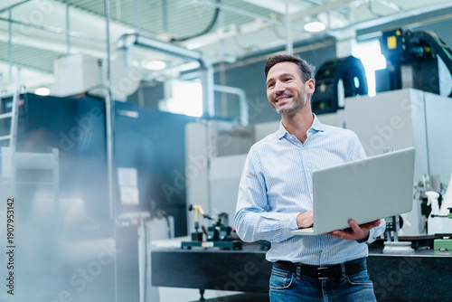 Happy mature businessman holding laptop while working in industry