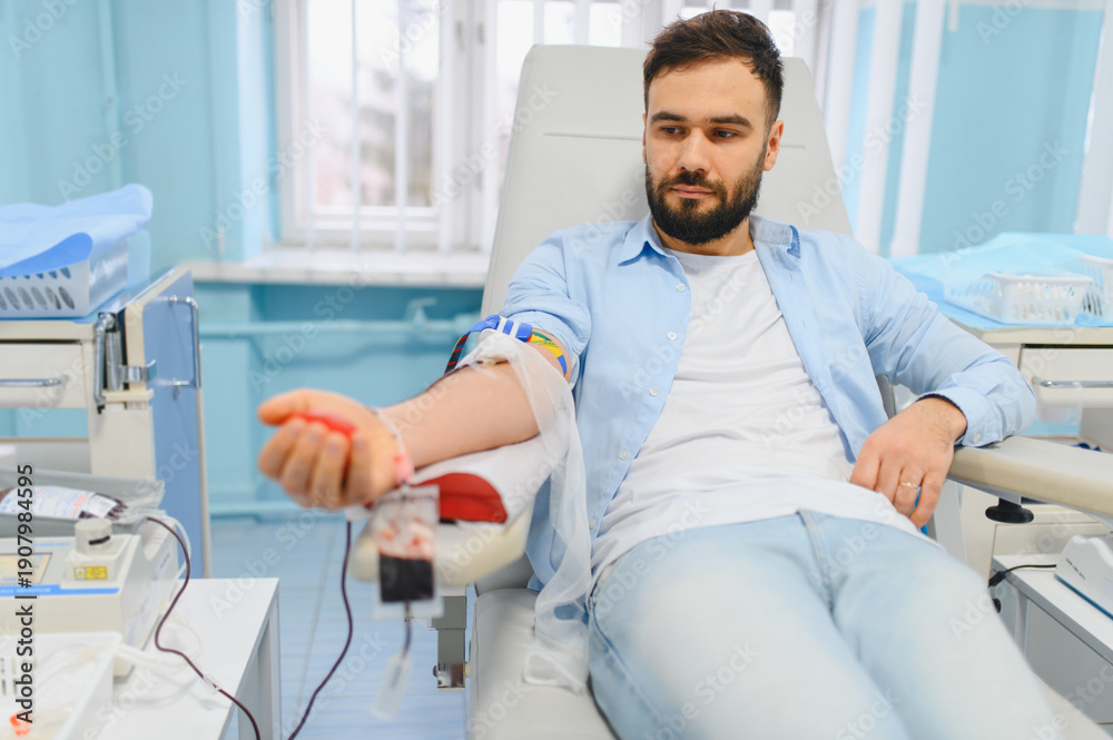 Fototapeta premium Young man donating blood in medical clinic for charity