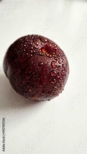 Foto Round plum with deep blue-red color, placed on a plain white surface