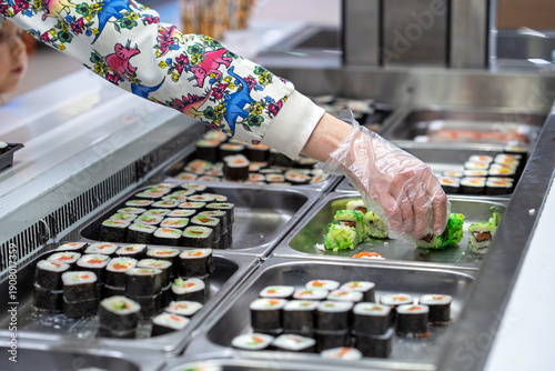 Buying sushi rolls in a store. A customer's hand in a disposable glove selects sushi rolls in a store.