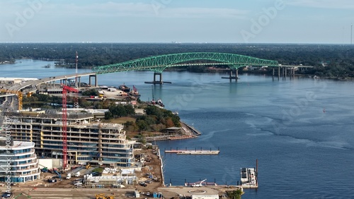 Aerial view of the bright green Mathews Bridge arches over the sparkling St. Johns River near the developing riverfront, Jacksonville, Florida, United States.