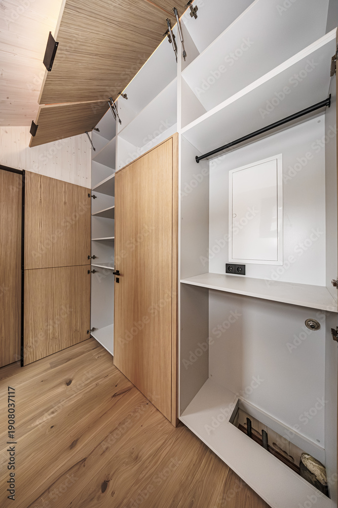 Fototapeta premium Built-in storage system featuring open wood-paneled cabinets and clean white shelves in a minimalist interior. Hardwood floors and concealed hinges. No logos visible