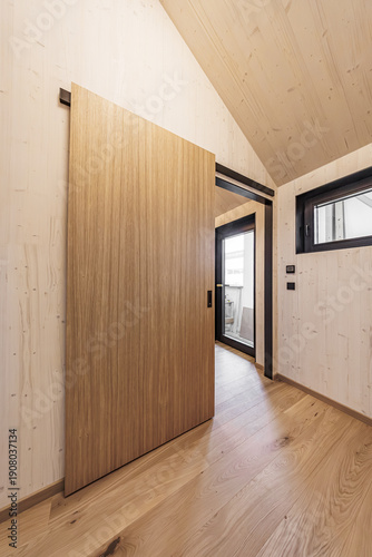 Slika na platnu Bright room with a natural wood sliding door, light wooden walls and ceiling, black-trimmed windows, and hardwood flooring