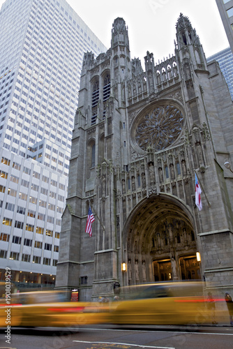 New York, United States - 28 January 2010: View of a Gothic Revival church facade juxtaposed against a modern skyscraper, a vibrant yellow taxi blurs past, hinting at the city's relentless pace.