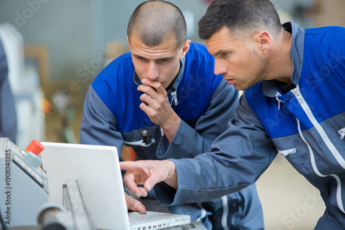 handsome auto mechanic and apprentice with laptop