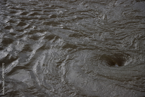Swirling whirlpool in textured surface of brown river water