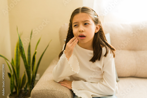 Tableau sur toile Little girl covering cheek with hand, suffering from toothache pain at home, nee