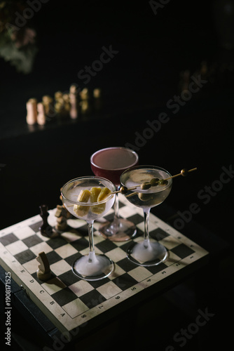 Wallpaper Mural Three Martini cocktails, two differently garnished dirty martinis and a twist on espresso martini, standing on a wooden chess board in the dark room, close up view  Torontodigital.ca