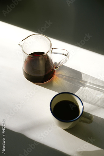 Wallpaper Mural A cup of freshly brewed hot black filter coffee and a server full of it, standing on the white surface in the sun, making soft golden shades, top view, flat lay, vertical image  Torontodigital.ca