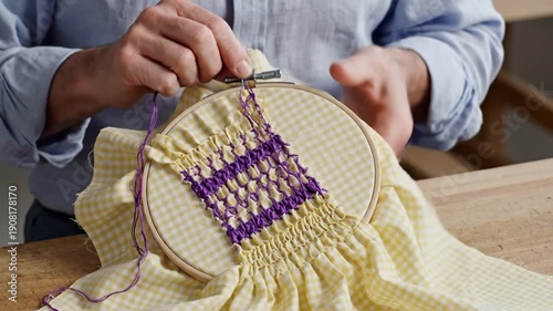 Man's hands smocking yellow gingham fabric with purple thread
