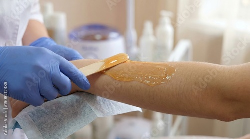 
Esthetician in blue gloves performing professional waxing procedure on client's arm. Close-up of gentle hair removal technique in modern beauty salon. Body care and grooming service concept