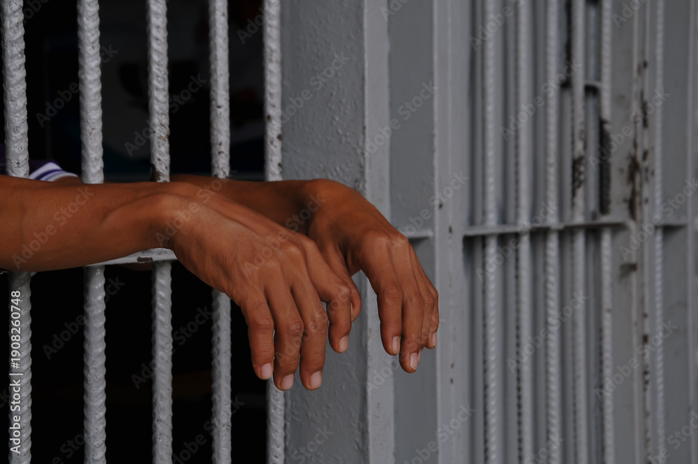 Obraz premium prisoner's hands behind bars at black background