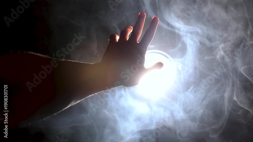 A man's hand reaches for the light, a video concept. To reach for the light, to strive for the truth, the light of a powerful spotlight hits the frame, volumetric lighting, the rays shine through the 