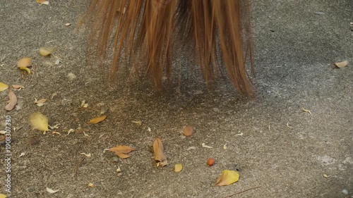 Coconut broom sweeping dry leaves on a concrete ground creating a coarse scratching and rustling sound