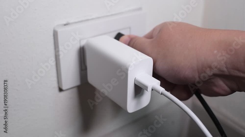 Hand gently wiggling and pulling an electrical plug from a wall socket creating a plastic friction sound
