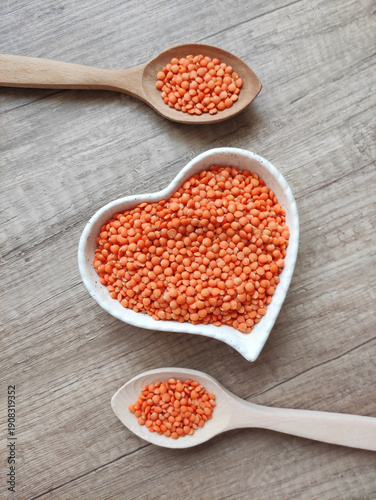 Dried small red lentils in a decorative plate and wooden spoons on a wooden background