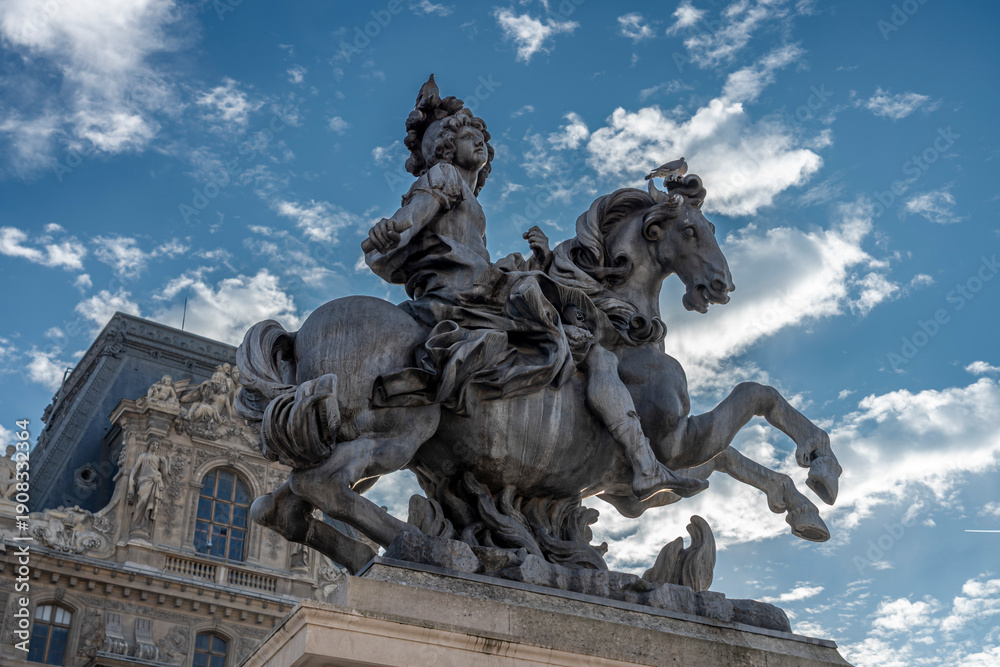 Fototapeta premium Paris, France - 10 11 2025: Detail view of the statue of Louis XIV and buildings of Le Louvre Museum behind