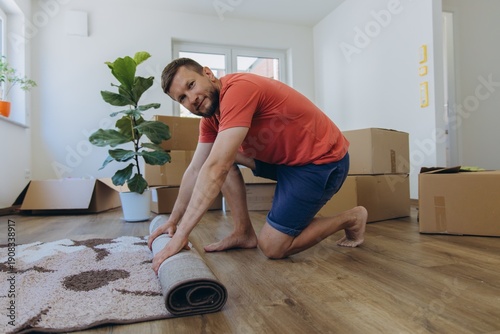Man rolling carpet while unpacking in new home during relocation