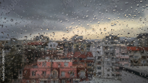 Moody raindrops on glass with a blurred urban landscape and grey clouds. Perfect for autumn, melancholy, or cozy interior concepts with a city view background