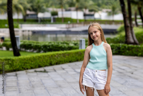 beautiful caucasian girl smiling outdoor at hot summer day. Child posing in tropical garden in luxury hotel