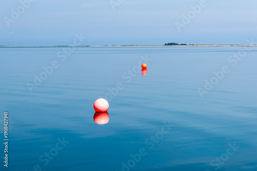 Minimalist seascape with orange buoys on calm blue water, Denmark coast.