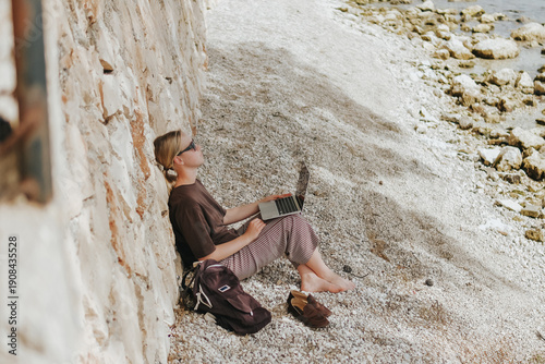 Foto Young woman working remotely by the sea with a laptop and solar panel, embracing sustainable travel, mindful lifestyle and digital freedom