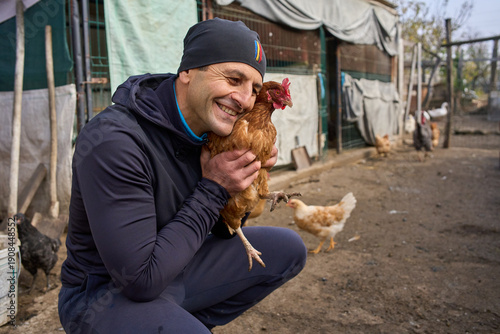 Farmer cuddling hen in backyard coop