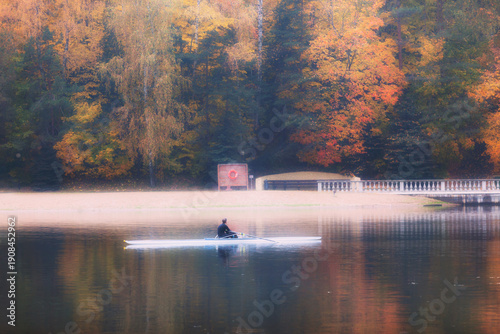 A sportsman in the rowing boat amidst the river pausing to watch autumn trees