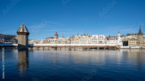 Kapellbrücke in Lucerne in winter under bright sunshine and a steel-blue sky, a famous tourist landmark with Mount Pilatus rising in the background.