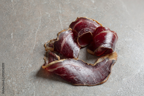Elegant curls of Spanish cured beef cecina arranged in a refined circular composition on a natural limestone stone surface. High-end artisanal charcuterie with rich texture, deep tones and minimalist 