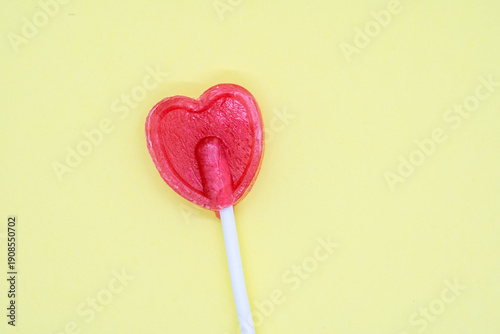 Red heart-shaped lollipop creating a sweet love concept on a yellow background