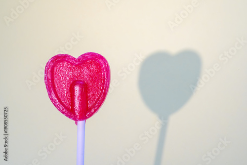 Pink heart-shaped lollipop casting a heart and stick shadow on a light background